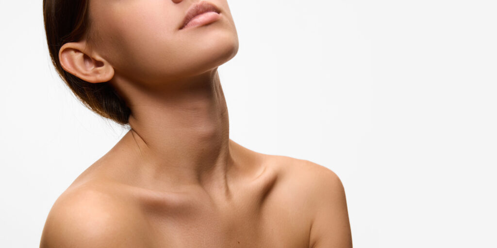 Close-up of woman's neckline and jawline, highlighting her smooth skin and natural elegance against white studio background. Concept of natural beauty.
